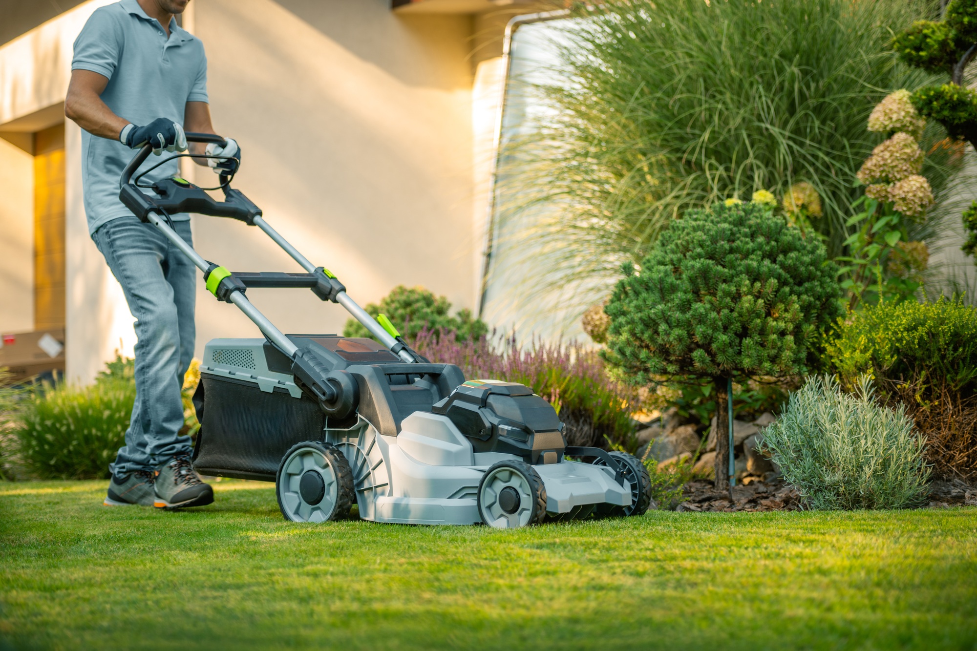 A Person Mowing the Lawn in a Residential Garden During a Sunny Summer Afternoon